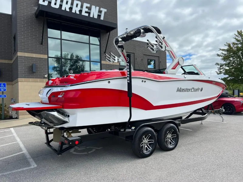 Slide: The Image of 2023 MasterCraft X24 boat on trailer, red and white design, parked outside a building. - 3