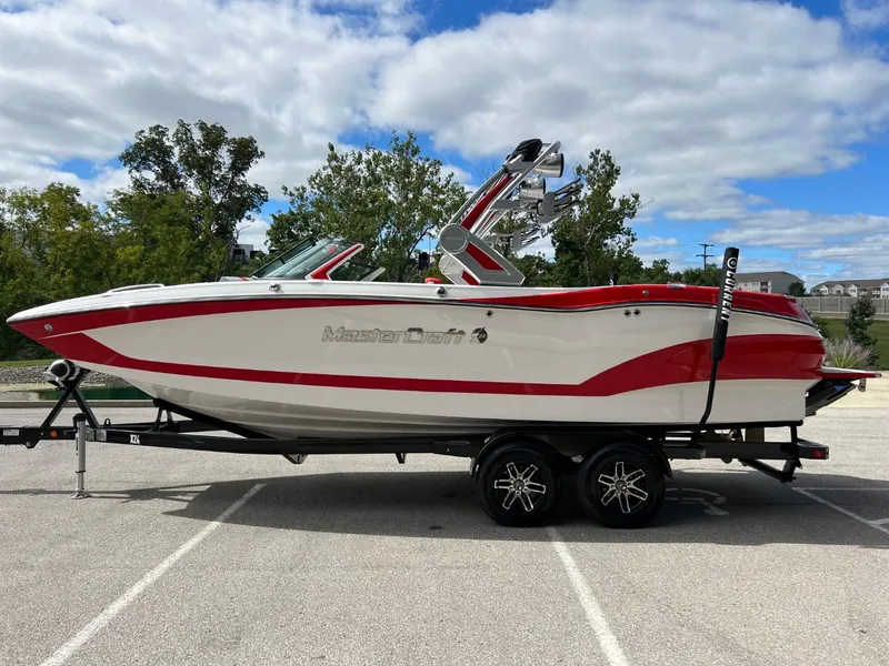 Slide: The Image of 2023 MasterCraft X24 boat with red and white design on a trailer in a parking lot. - 6