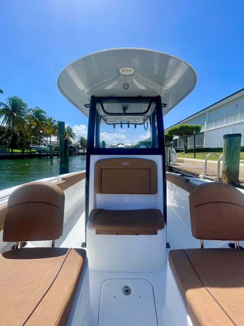 Slide: The Image of 2023 Sea Hunt Ultra 255 SE boat interior with seating, docked by palm trees. - 7