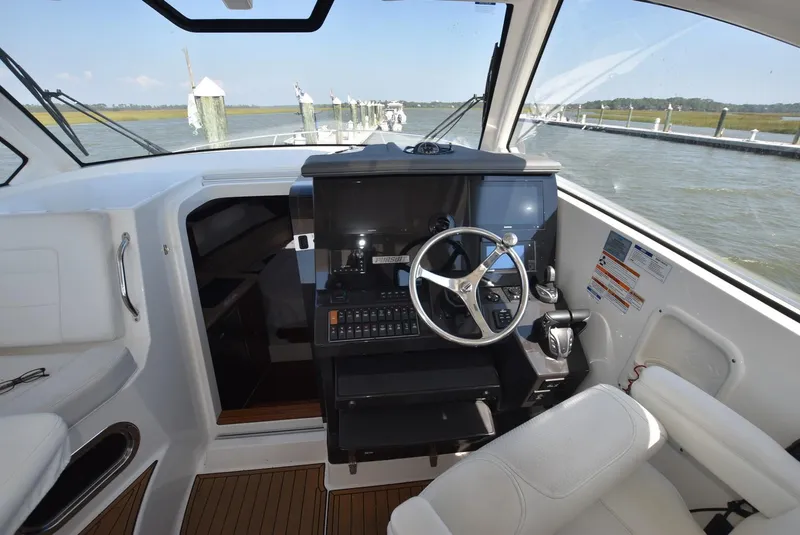 Slide: The Image of 2022 Pursuit OS 355 Offshore helm with steering wheel and control panel, overlooking marina. - 8