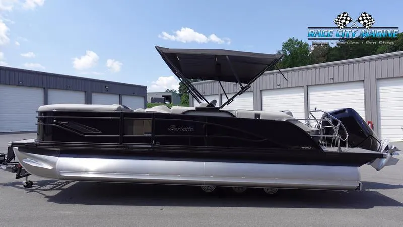 Slide: The Image of 2025 Barletta X23U pontoon boat with canopy, parked outdoors. - 1
