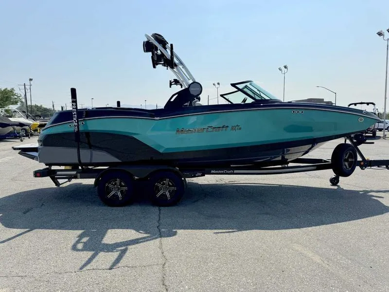 Slide: The Image of 2025 MasterCraft NXT22 boat on trailer, teal and black design, parked outdoors. - 5