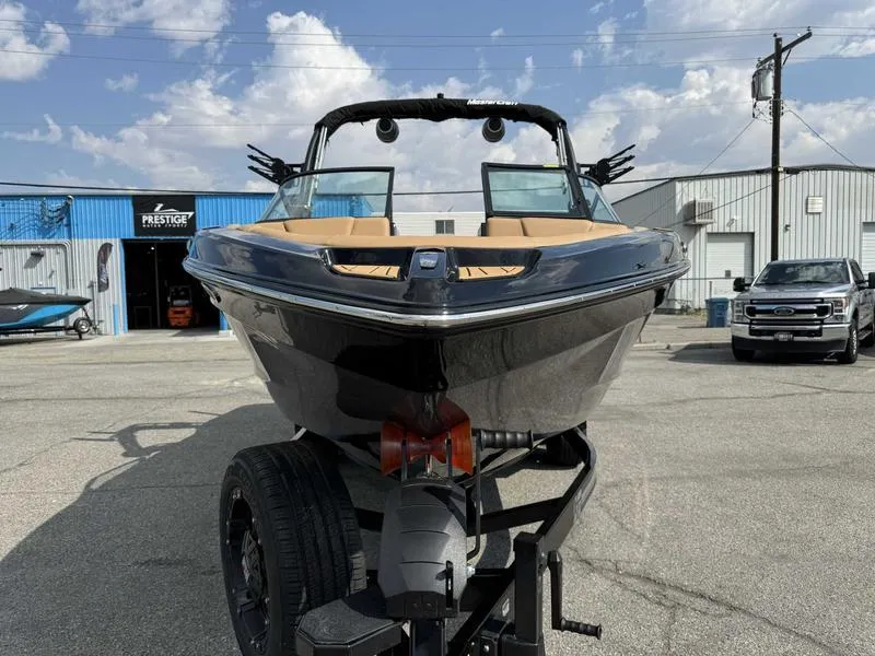 Slide: The Image of 2025 MasterCraft XT23 boat on trailer, parked outdoors under a partly cloudy sky. - 14