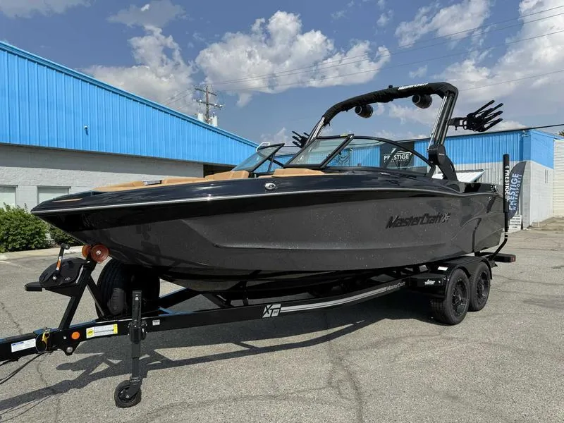 Slide: The Image of 2025 MasterCraft XT23 boat on trailer, parked outdoors under a partly cloudy sky. - 15