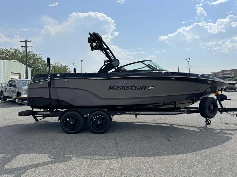 Slide: The Image of 2025 MasterCraft XT23 boat on trailer, parked outdoors under a partly cloudy sky. - 5