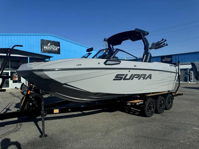 Slide: The Image of 2025 Supra SE boat on trailer at dealership, blue building background. - 16