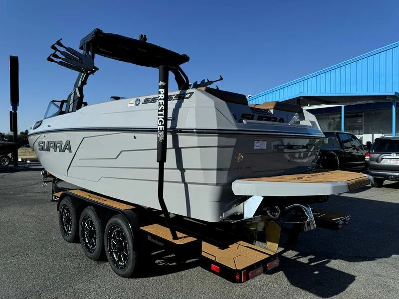 Slide: The Image of 2025 Supra SE boat on trailer, gray exterior, parked outdoors near blue building. - 4