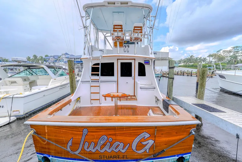 Slide: The Image of 1982 Hatteras 46 Convertible boat docked, rear view with wooden deck and fishing chairs. - 49
