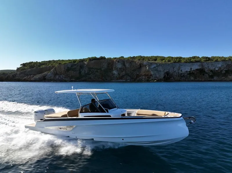 Slide: The Image of 2025 STERK 31 WB Sport boat cruising on clear blue water near rocky coastline. - 16