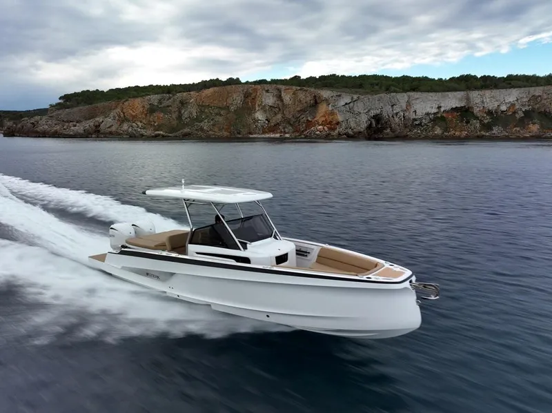 Slide: The Image of 2025 STERK 31 WB Sport boat cruising on calm waters near rocky coastline. - 17