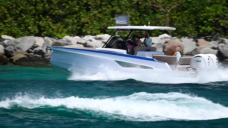 Slide: The Image of 2025 STERK 31 WB Sport boat cruising on clear blue water near rocky shoreline. - 4