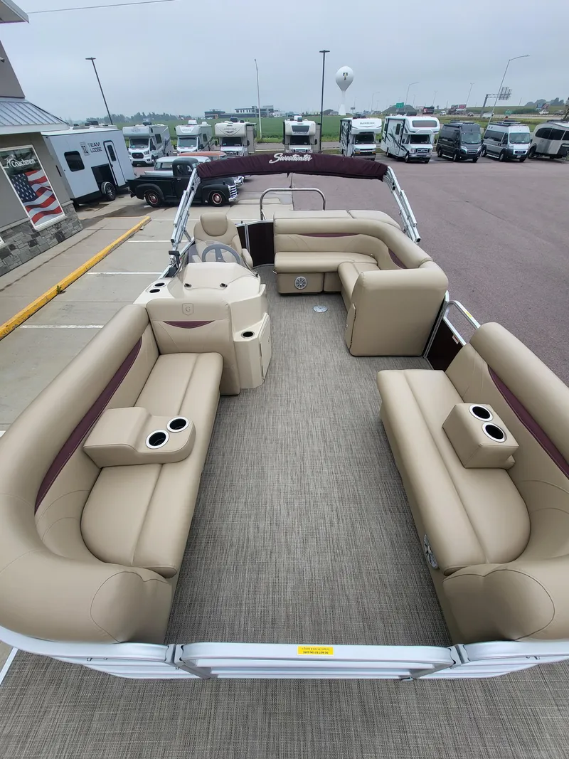 Slide: The Image of 2018 Sweetwater CRUISER pontoon boat with beige seating and cup holders, parked at a dealership. - 6