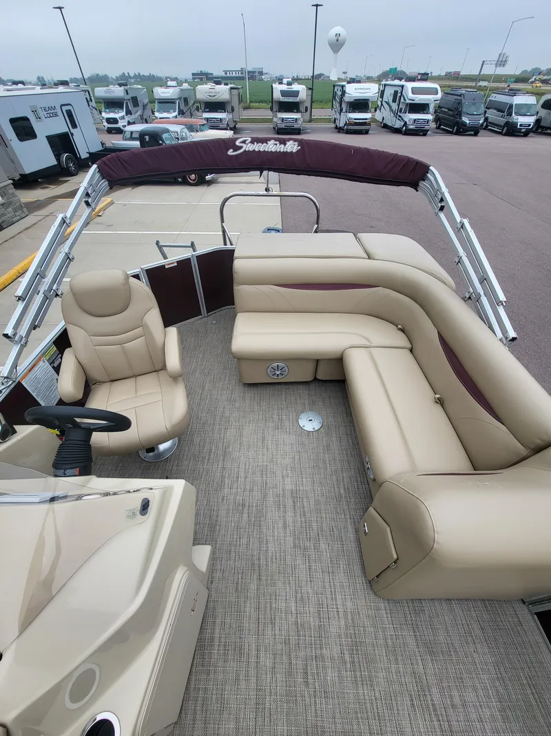 Slide: The Image of 2018 Sweetwater CRUISER boat with beige seating and maroon canopy, parked near RVs. - 7