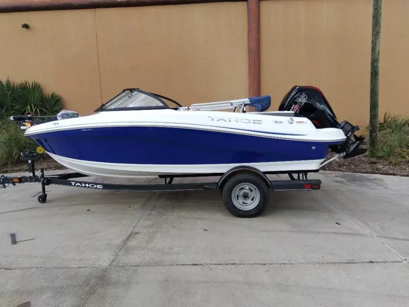 The Image of 2024 Tahoe 185 S boat on trailer, blue and white design, parked outdoors. - 0