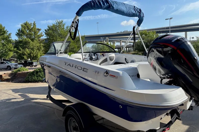 Slide: The Image of 2024 Tahoe 185 S boat with blue and white design, parked outdoors under a clear sky. - 5