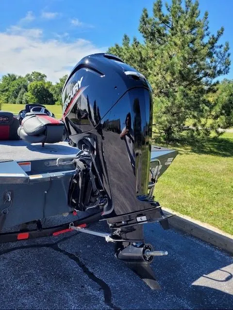 Slide: The Image of 2024 Ranger RT188C boat with Mercury outboard motor, parked on pavement near green trees. - 2