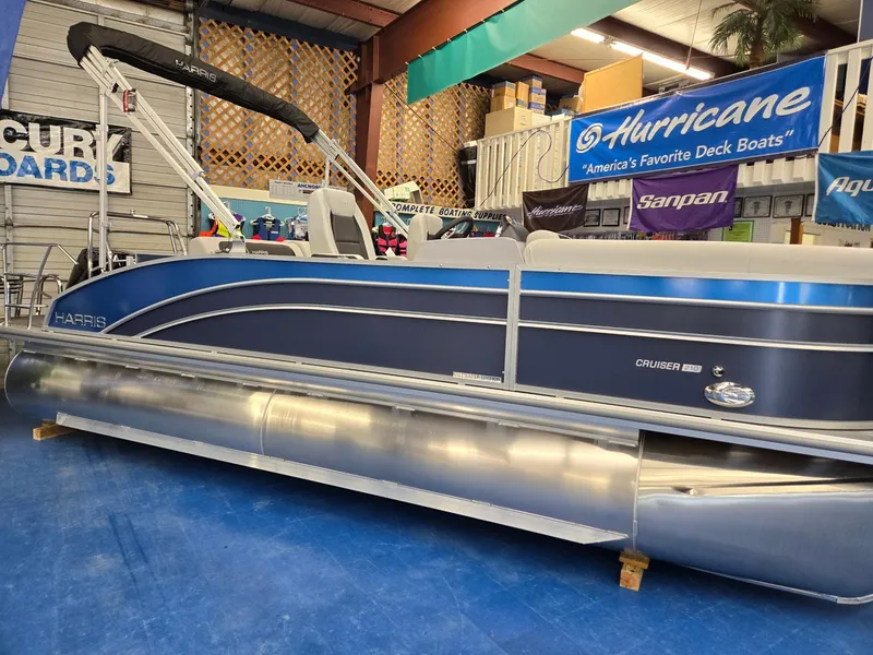 Slide: The Image of 2025 Harris Cruiser 210 pontoon boat displayed indoors with promotional banners. - 2