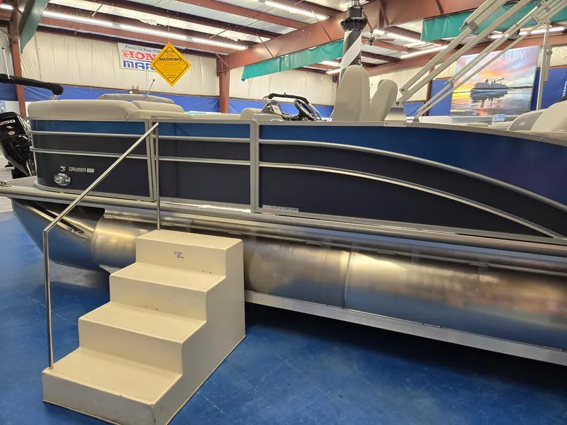 Slide: The Image of 2025 Harris Cruiser 210 pontoon boat displayed indoors with steps for access. - 5