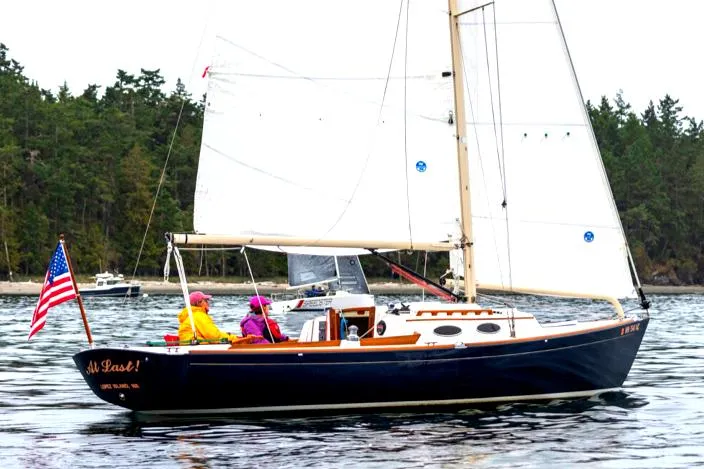 Slide: The Image of 2005 Express Alerion sailboat on water with American flag, forested shoreline in background. - 1