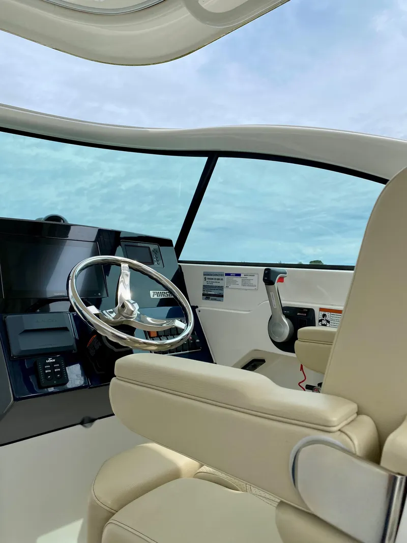 Slide: The Image of 2021 Pursuit DC 235 Dual Console boat interior with steering wheel and beige seating. - 12
