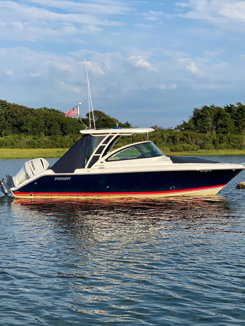 Slide: The Image of 2021 Pursuit DC 235 Dual Console boat on calm water, with scenic background. - 3