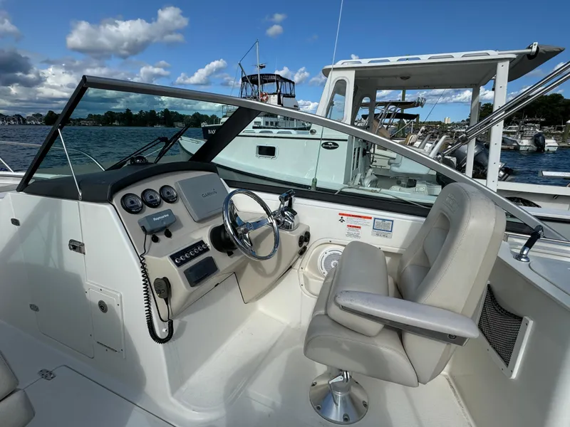 Slide: The Image of 2013 Boston Whaler 270 Vantage boat cockpit with steering wheel and controls, docked by the water. - 16