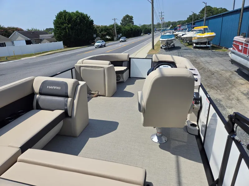 Slide: The Image of 2025 Harris Cruiser 210 pontoon boat interior with beige seating, parked near a road. - 24