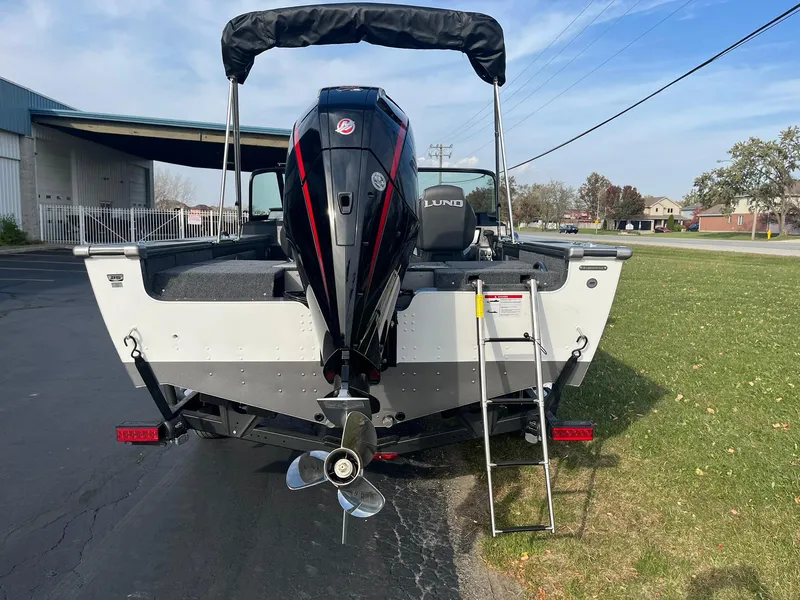 Slide: The Image of 2025 Lund 1875 Pro-V boat with outboard motor and ladder, parked outdoors. - 3