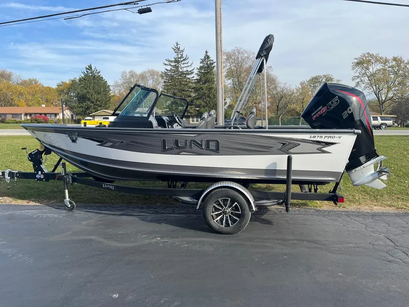 Slide: The Image of 2025 Lund 1875 Pro-V boat on trailer, parked outdoors on a sunny day. - 4