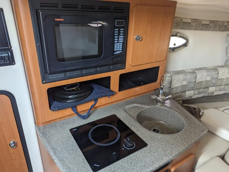 Slide: The Image of 2004 Crownline 250 CR boat interior with kitchenette, featuring microwave, stove, and sink. - 29