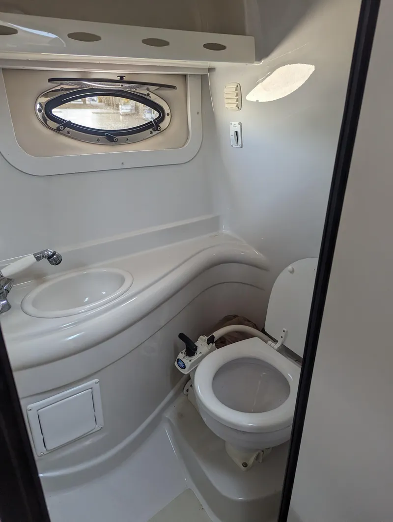 Slide: The Image of 2004 Crownline 250 CR boat bathroom with sink, toilet, and porthole window. - 34