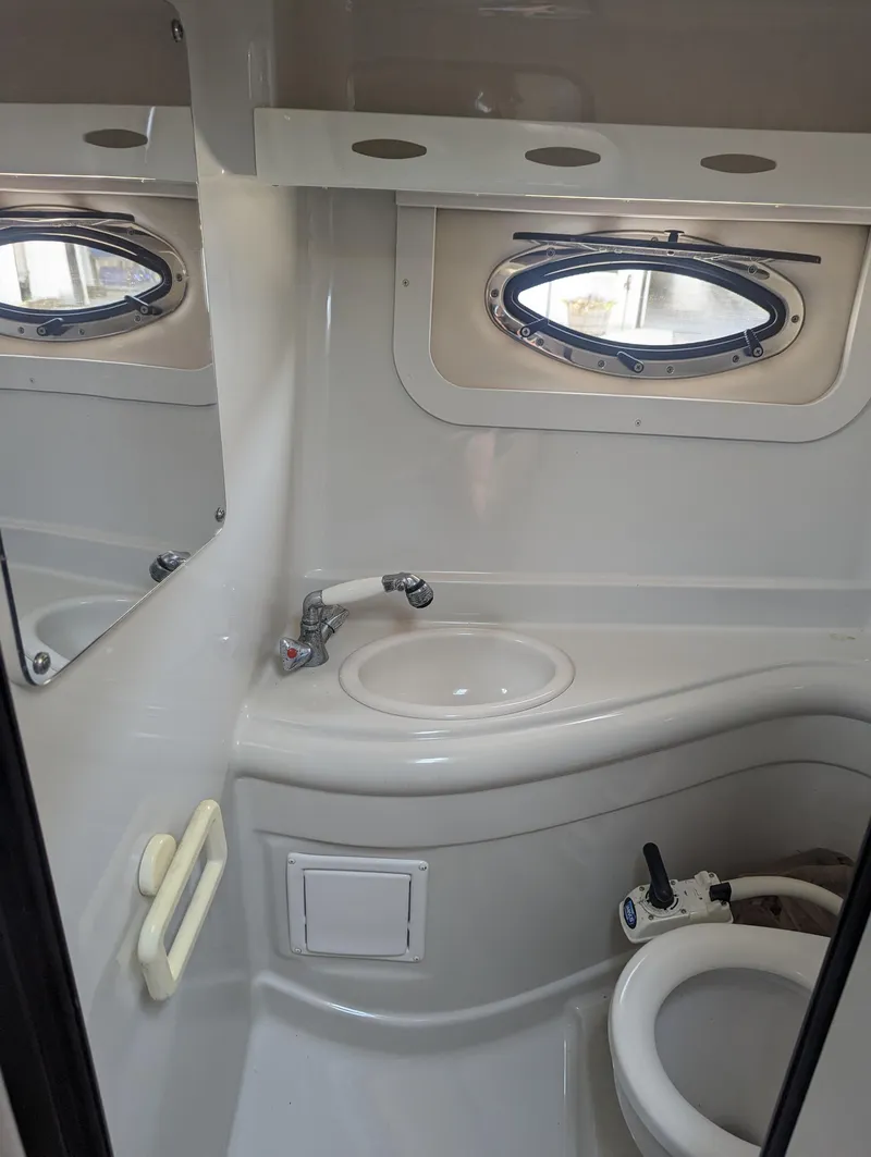 Slide: The Image of 2004 Crownline 250 CR boat bathroom with sink, toilet, and porthole window. - 35