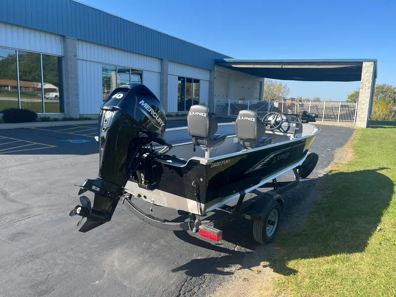 Slide: The Image of 2025 Lund 1600 Fury SS boat with Mercury engine on trailer, parked outside a building. - 2
