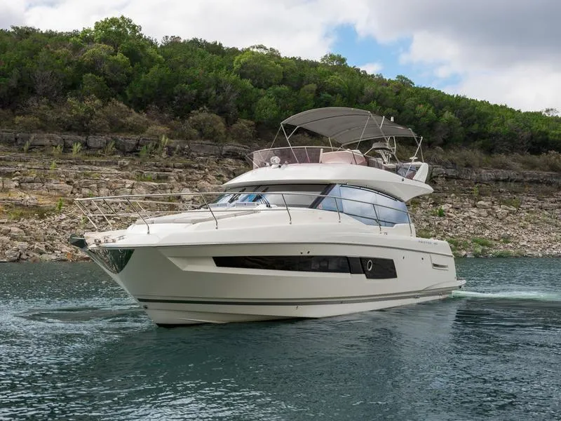 The Image of 2022 Prestige 460F yacht cruising on a scenic lake with lush greenery. - 0