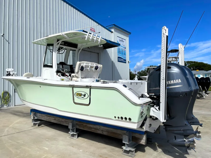 Slide: The Image of 2022 Sea Hunt Gamefish 25 boat with Yamaha engines, parked outside a metal building. - 0