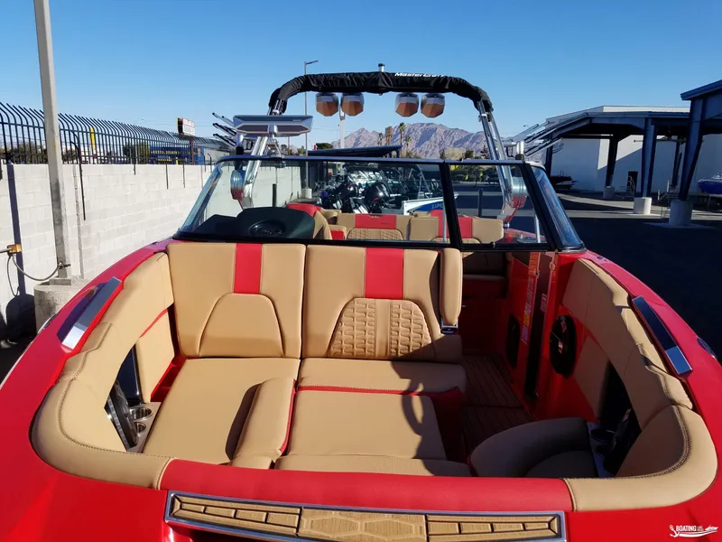 Slide: The Image of 2021 MasterCraft X26 boat interior with tan and red seating, parked outdoors. - 25