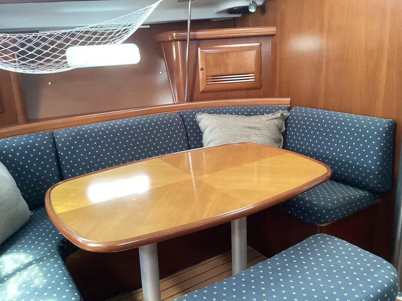 Slide: The Image of Cozy dining area in 2002 Beneteau 393 sailboat with wooden table and blue cushioned seating. - 10
