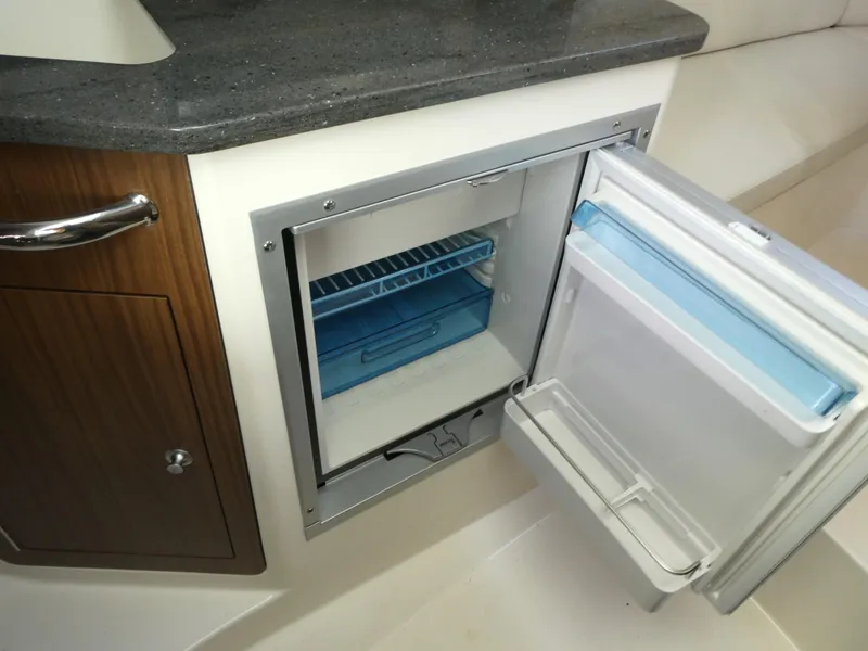 Slide: The Image of 2024 Boston Whaler 285 Conquest interior with open mini fridge and wooden cabinetry. - 14
