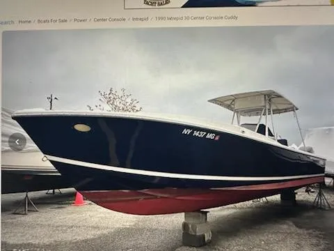 Slide: The Image of 1990 Intrepid 30 Console Cuddy boat on display, blue hull, red bottom, parked on blocks. - 2