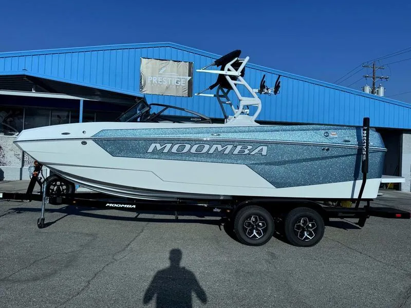 Slide: The Image of 2025 Moomba Max boat on trailer, parked outside a blue building. - 0
