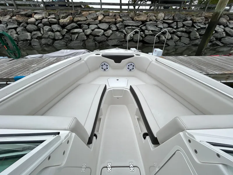 Slide: The Image of 2024 Sailfish 226 DC boat interior with white seating and speakers, docked by a stone wall. - 11