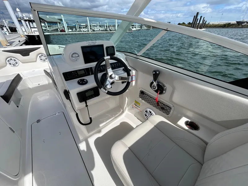Slide: The Image of 2024 Sailfish 226 DC boat interior with steering wheel and dashboard, docked by the water. - 10
