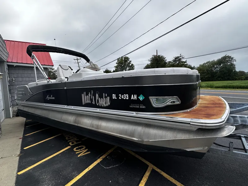 Slide: The Image of 2014 Avalon Catalina Quad Lounge 24' Triple Toon boat on trailer, black exterior, wooden deck. - 8