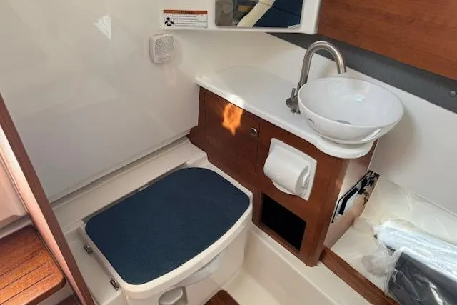 Slide: The Image of 2026 Pursuit S 328 Sport boat bathroom with sink, toilet, and wooden cabinetry. - 18