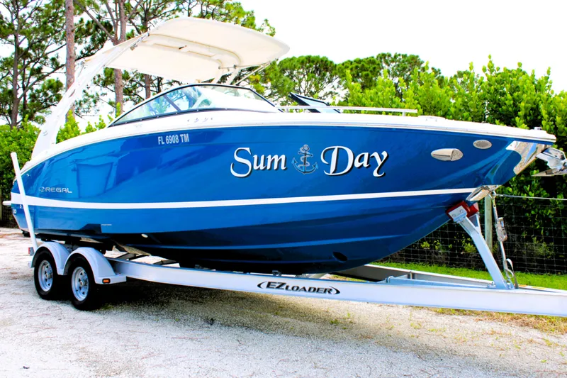 Slide: The Image of 2023 Regal LX6 boat named "Sum Day" on trailer, parked outdoors. - 2