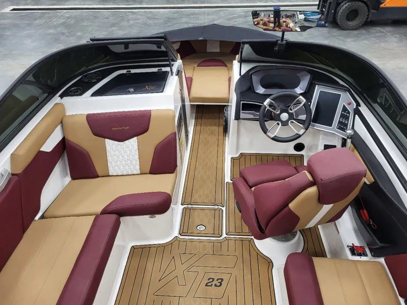 Slide: The Image of 2022 MasterCraft XT23 boat interior with maroon and tan seating, modern dashboard, and wood-style flooring. - 16