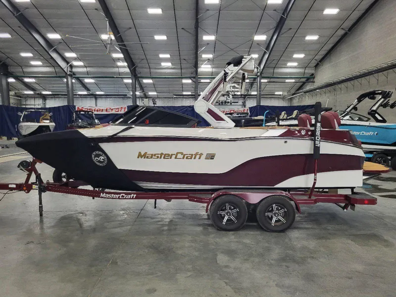 Slide: The Image of 2022 MasterCraft XT23 boat in showroom, side view, maroon and white design. - 7