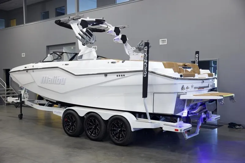 Slide: The Image of 2025 Malibu M242 boat on trailer in showroom, sleek design, white exterior. - 4