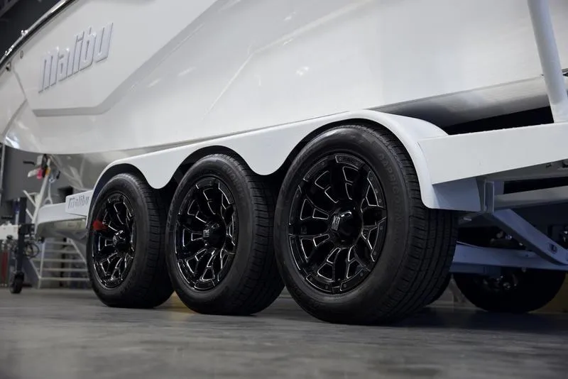 Slide: The Image of 2025 Malibu M242 boat trailer with triple black wheels in a showroom. - 8