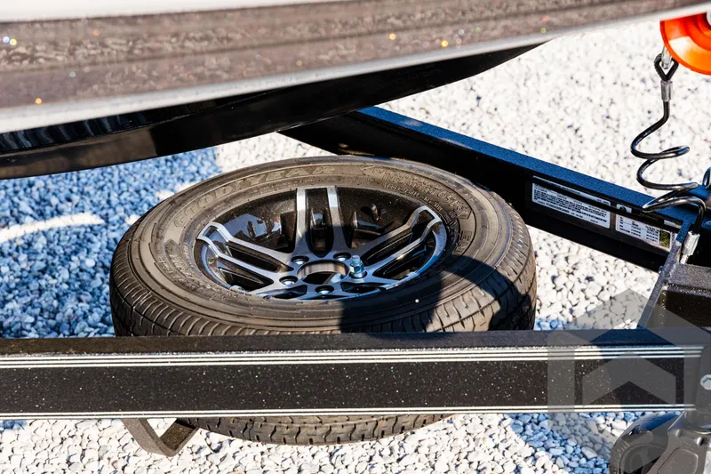 Slide: The Image of Spare tire on Skeeter ZXR 20 boat trailer, 2025 model, on gravel surface. - 11